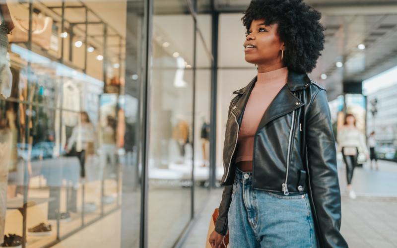 Zwarte jonge vrouw staat buiten voor de etalage van een kledingwinkel Zwarte jonge vrouw staat buiten voor de etalage van een kledingwinkel