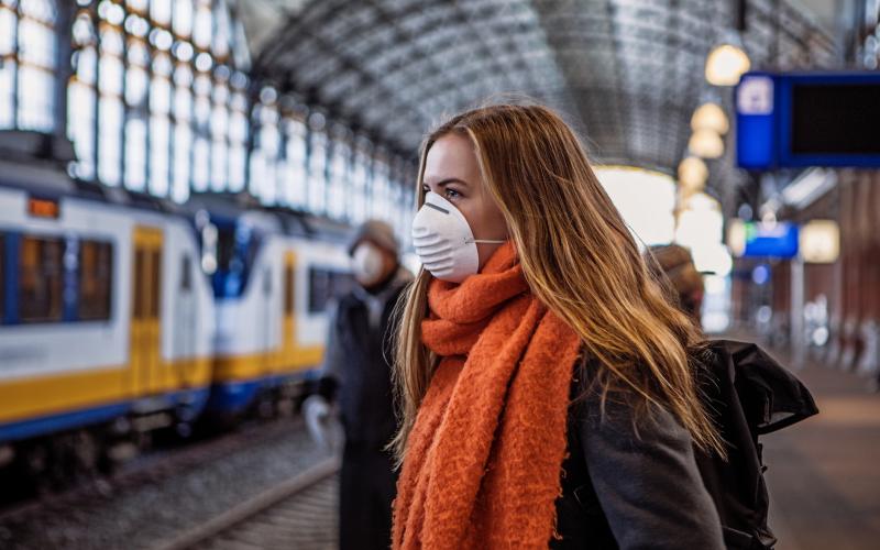 Jonge vrouw met een mondkapje wacht op een trein