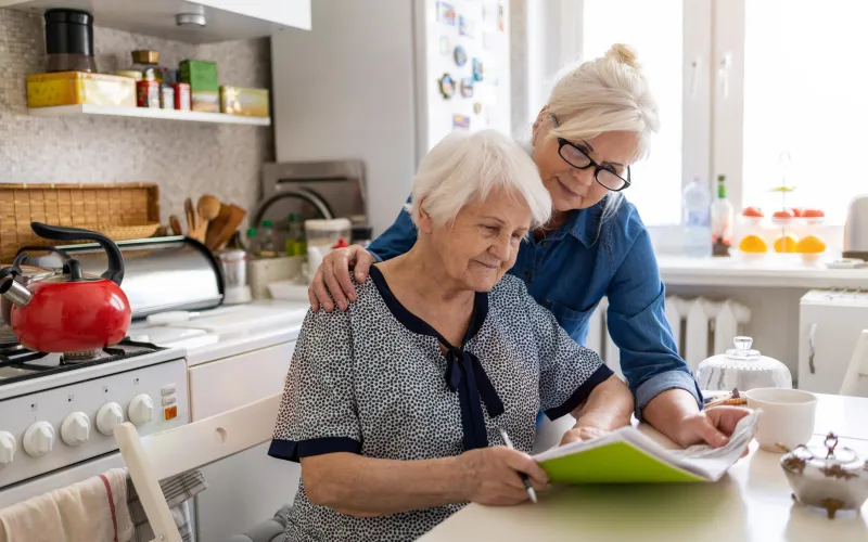 Een jongere vrouw helpt een oudere vrouw met een formulier