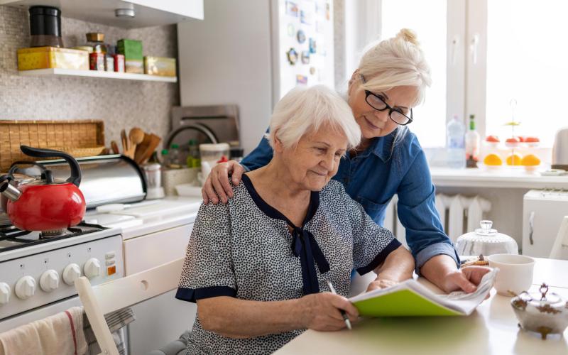 Een jongere vrouw helpt een oudere vrouw met een formulier