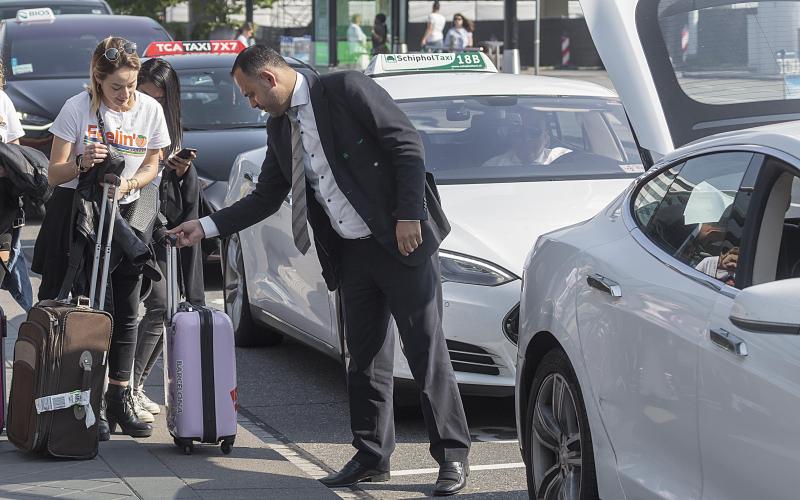 Een taxichauffeur staat bij zijn taxi samen met een vrouw met koffers.