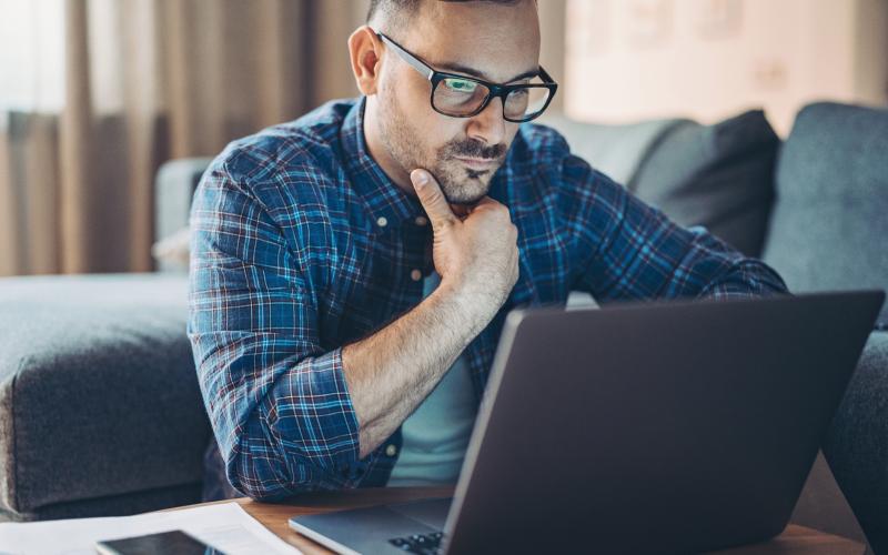 Man van middelbare leeftijd met bril en geruite blouse kijkt zorgelijk naar zijn laptop.