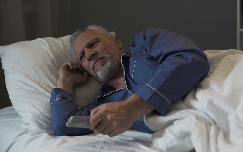 Senior man met grijs haar en grijze baad ligt wakker in bed