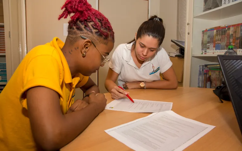 Een leerkracht legt een Caribische student iets uit op een papiertje