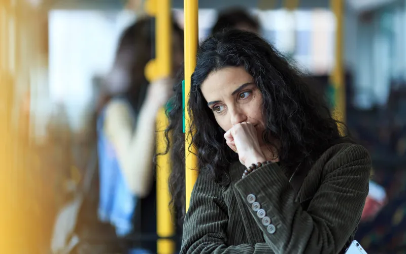Vrouw met zwart krullend haar staat in de metro en kijkt bedenkelijk voor zich uit