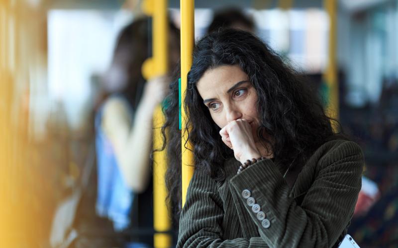 Vrouw met zwart krullend haar staat in de metro en kijkt bedenkelijk voor zich uit