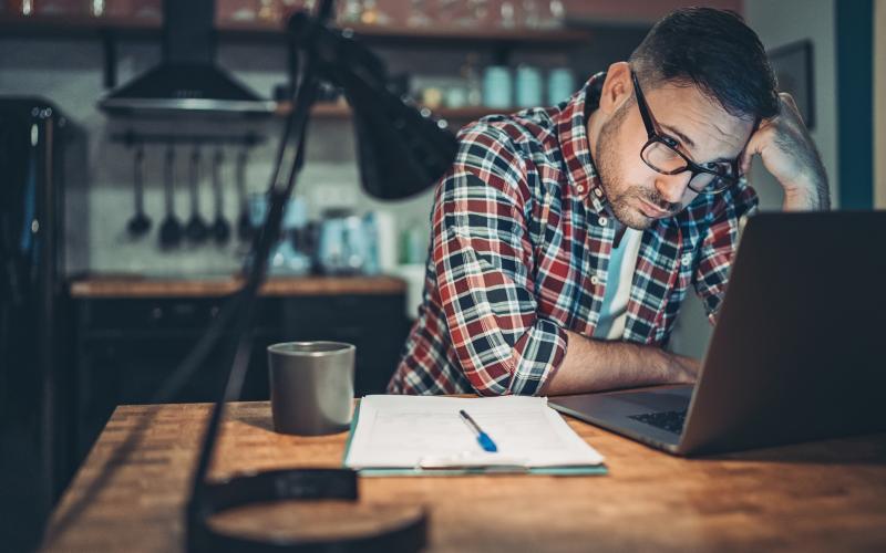 Volwassen man met bril en blokjesblouse zit gefrustreerd achter zijn laptop