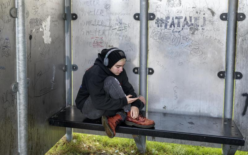 Jongere met koptelefoon zit op een bankje bij een hangplek Jongere met koptelefoon zit op een bankje bij een hangplek