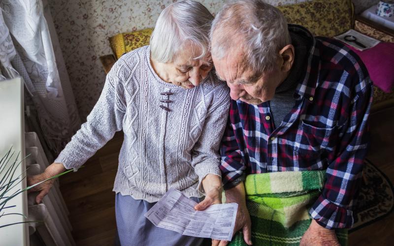 Ouder echtpaar zit naast elkaar bij de verwarming en bekijkt de energierekening