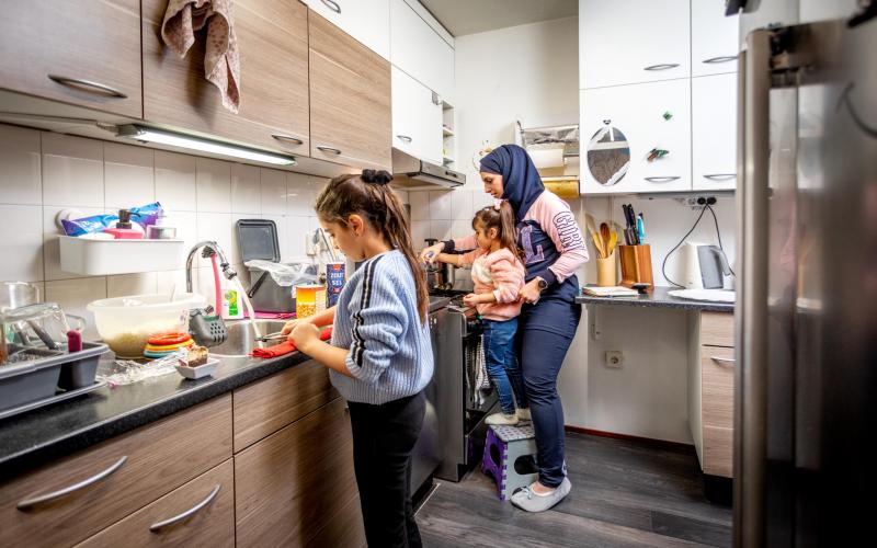 Vrouw met migratieachtergrond staat in de keuken met haar twee kinderen.