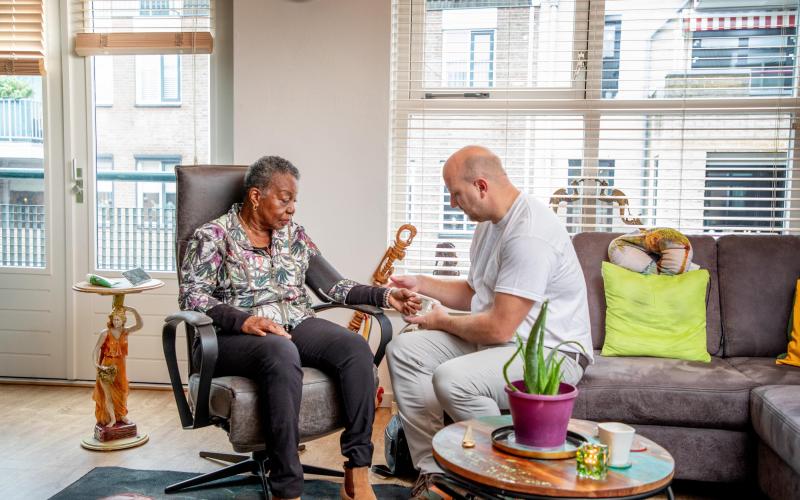 Een thuiszorgmedewerker helpt een oudere vrouw bij haar thuis met haar bloeddruk