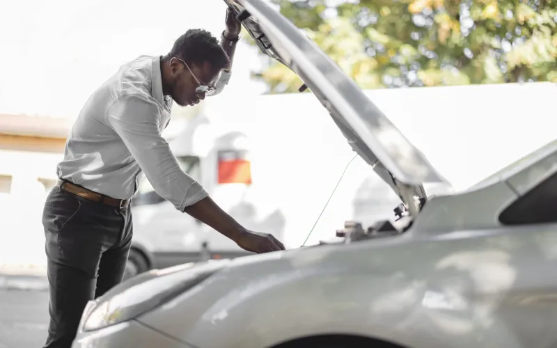 Man van middelbare leeftijd staat bij zijn auto. De motorkap is omhoog.