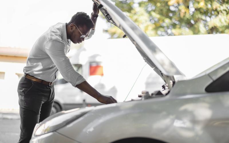 Man van middelbare leeftijd staat bij zijn auto. De motorkap is omhoog.