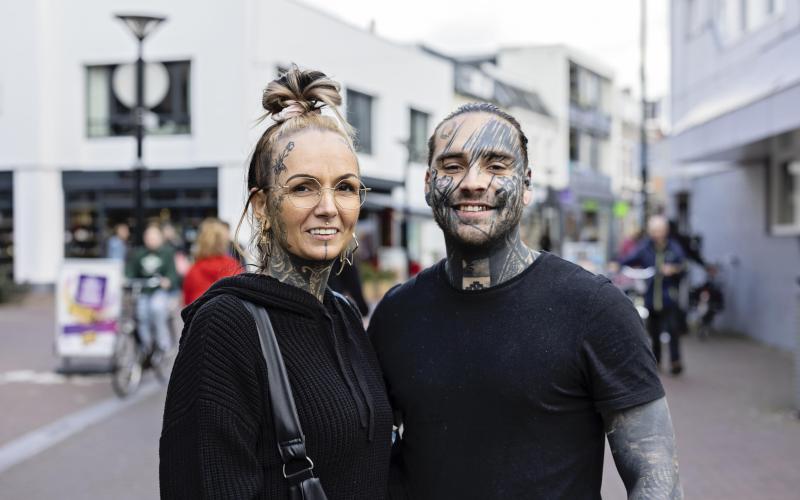 Jenny en William, een vrouw en man staan naast elkaar op straat. Ze zijn beiden zichtbaar getatoeëerd.