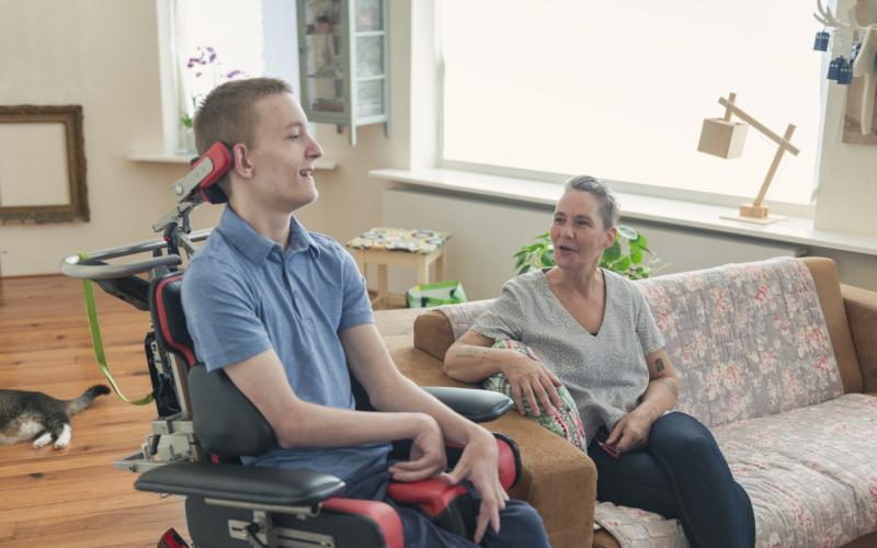 Een jongen in een elektrische rolstoel in gesprek met een vrouw op de bank ernaast Een jongen in een elektrische rolstoel in gesprek met een vrouw op de bank ernaast