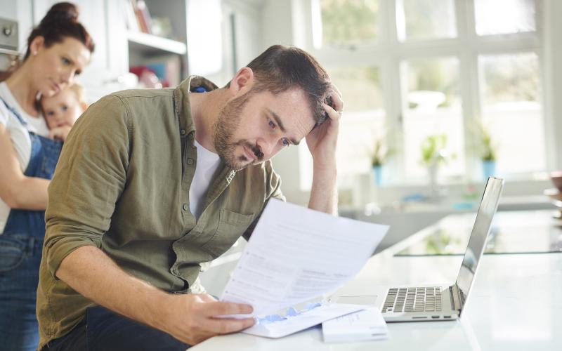 Man, zittend in keuken, kijkt bezorgd naar document in zijn hand Man, zittend in keuken, kijkt bezorgd naar document in zijn hand