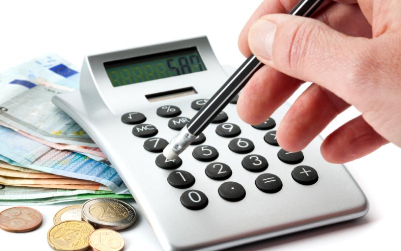 Foto van een rekenmachine op een stapel bankbiljetten en iemand die met een pen op de toetsen drukt