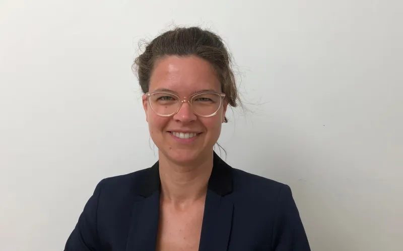 Sabine de Bruijn, een vrouw met bril en donkerbruin haar dat ze vast heeft. Ze draagt een zwarte blazer.