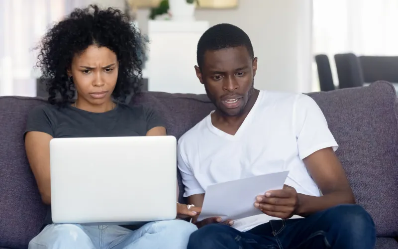 Echtpaar naast elkaar op de bank, kijkt verbaasd naar laptop