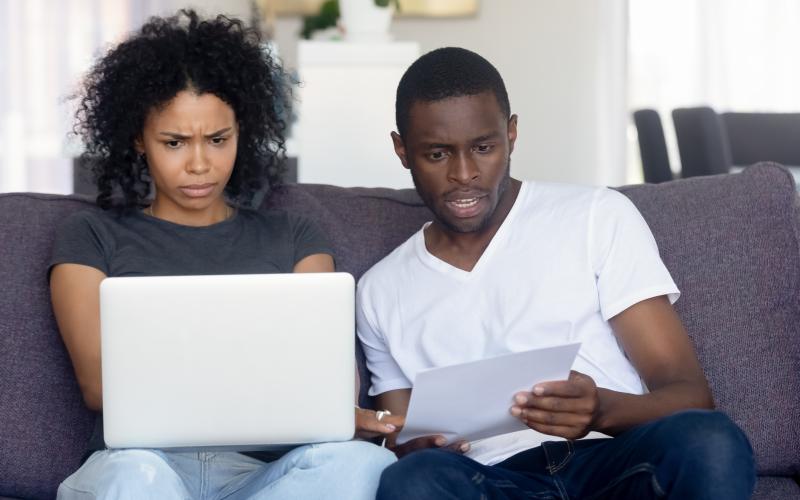 Echtpaar naast elkaar op de bank, kijkt verbaasd naar laptop Echtpaar naast elkaar op de bank, kijkt verbaasd naar laptop