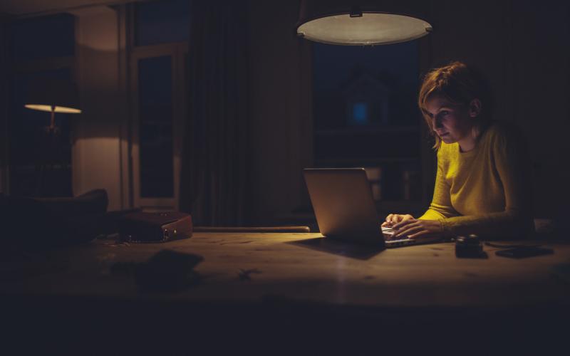 vrouw zit met haar laptop in donkere ruimte