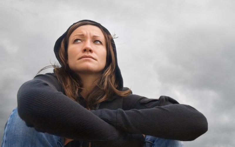 Zittende vrouw met zwarte trui en capuchon, de lucht is bewolkt Zittende vrouw met zwarte trui en capuchon, de lucht is bewolkt