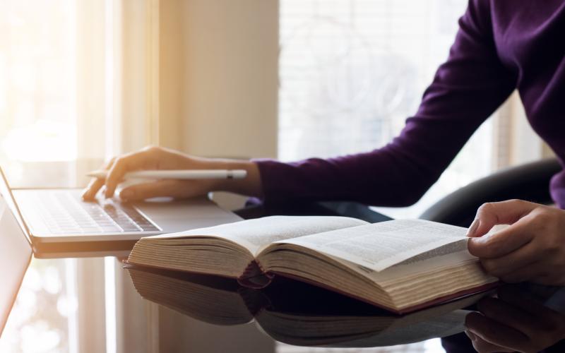 Een persoon gebruikt een woordenboek en laptop om te vertalen Een persoon gebruikt een woordenboek en laptop om te vertalen