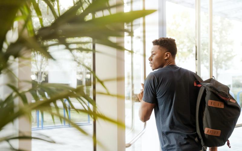 a young man with a backpack walks  through a glass entrance or door