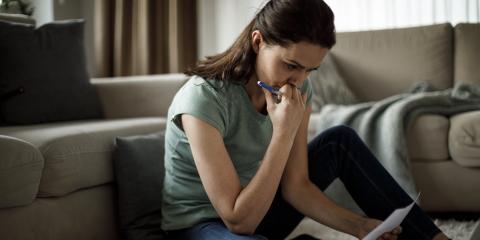 Vrouw zit op de grond en heeft papieren in haar hand. Voor haar staat ook een laptop.