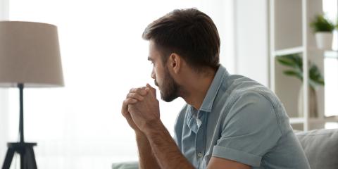 Een man van middelbare leeftijd met donker haar en een blauwe blouse zit op de bank. Hij kijkt nadenkend voor zich uit.