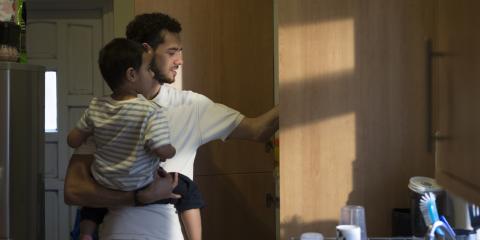Man draagt zoontje op zijn arm en pakt tegelijkertijd iets uit een keukenkastje.