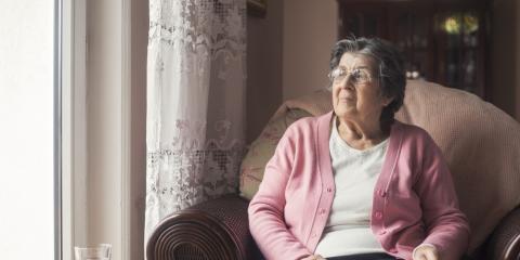 Senior vrouw zit op een stoel bij het raam. Ze heeft een boek vast.