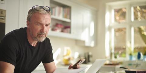 Man staat in zijn keuken en leest een brief. Hij houdt ook zijn telefoon vast.