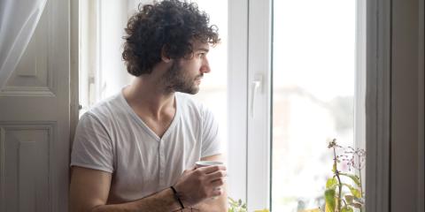 Man met koffie in hand kijkt uit zijn raam