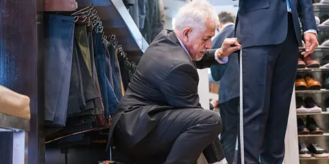 Een man laat zijn pak aanmeten. Je ziet de kleermaker en de benen van de man in pak