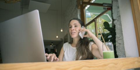 Vrouw zit in een café te bellen en kijkt op haar laptop.