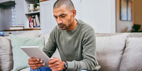 Man zit op de bank en kijkt serieus naar zijn tablet