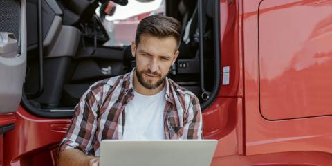 Man staat tegen zijn vrachtwagen aan en heeft een laptop vast