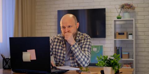 Man thuis achter laptop, hij kijkt bedenkelijk naar zijn scherm