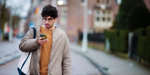 Een jonge man loopt op straat en kijkt naar zijn telefoon