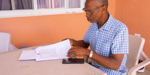 Man op Bonaire zit buiten aan een tafel en lees brieven van de overheid