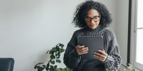 Vrouw met donkere krullen en grijze trui leest magazine online op tablet