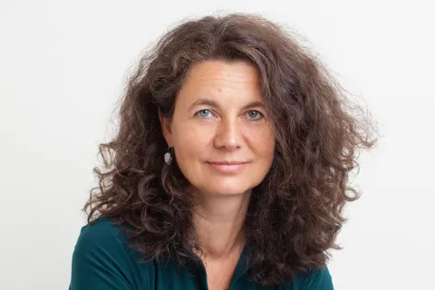 Irene Sluis, vrouw met lang donkerbruin krullend haar en blauwgroene blouse.