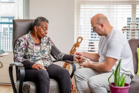 Zorgverlener helpt oudere vrouw thuis met opmeten bloeddruk