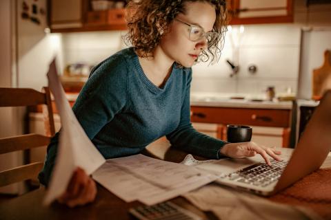 Vrouw met bril zit achter haal laptop en heeft papieren in haar hand