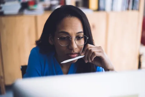 Vrouw met bril en tablet pencil in haar hand kijk op haar tablet of computerscherm. Ze is aan het werk.