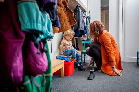 Moeder helpt kindje met het aantrekken van de schoenen. In de gang hangen veel jasjes