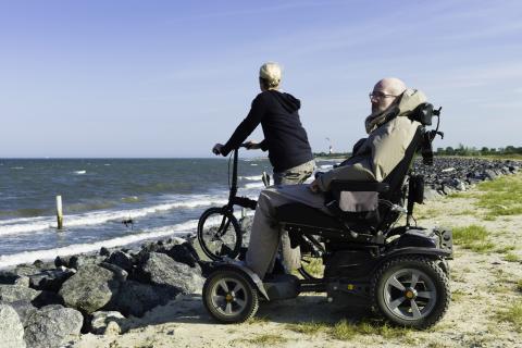 Man in rolstoel en vrouw op fiets kijken uit over de zee