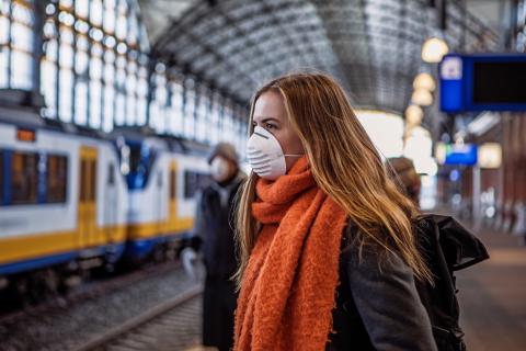 Vrouw staat met mondmasker op het station en wacht op de trein
