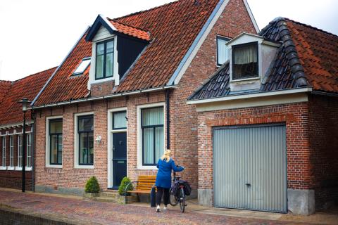 Oud huis met garage. Voor het huis staat een vrouw met fiets